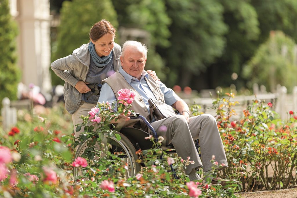 Pflegekraft und älterer Mann im Rollstuhl machen einen Spaziergang im Park