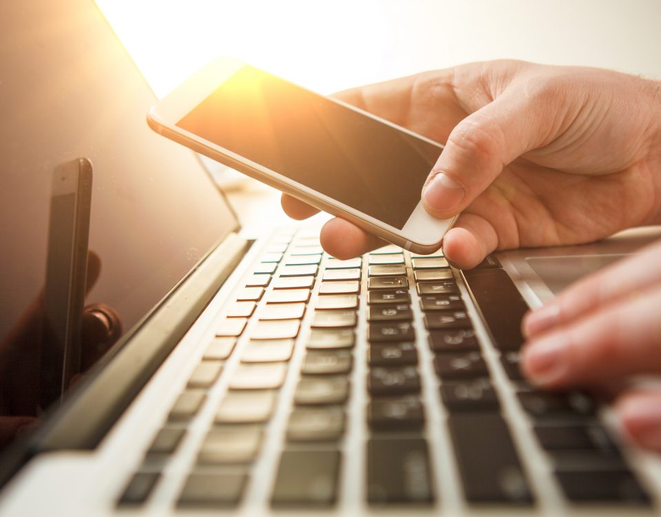 Zwei Hände auf einer Tastatur und einem Smartphone